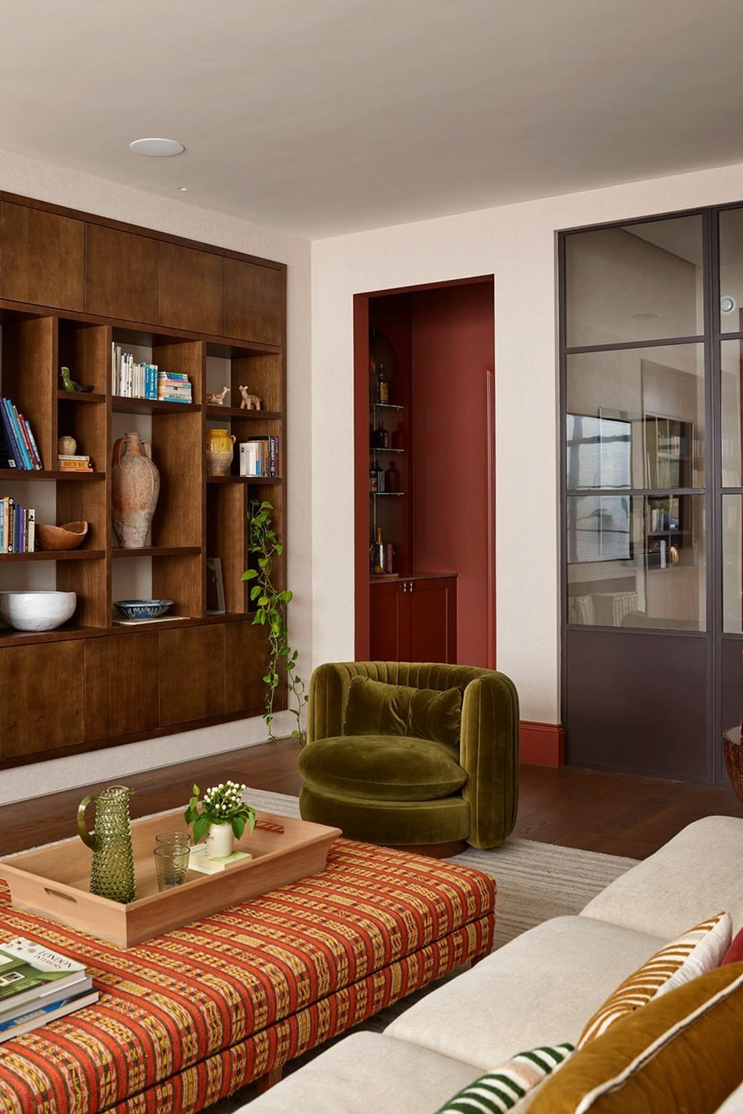 Salon avec fauteuil velours olive, ottoman ecossais et bibliotheque noyer